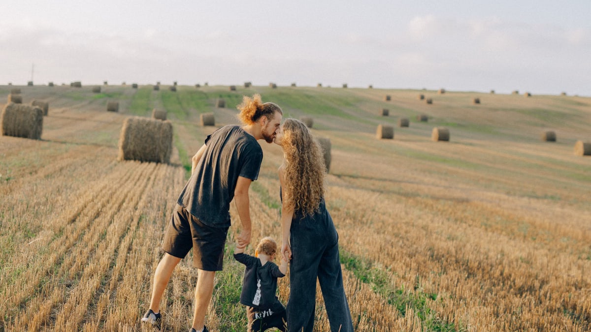 A couple with their child enjoy a sunny day in a wheat field, symbolizing love and joy.